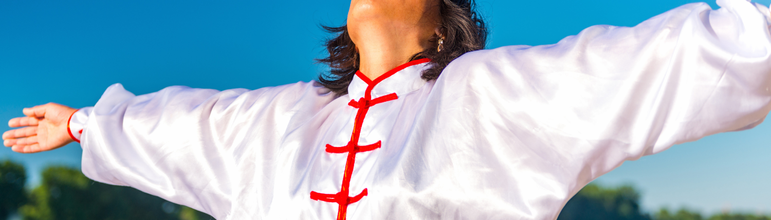 Personne en tenue blanche pratiquant le tai-chi bras ouverts sous un ciel bleu, vitalité et longévité